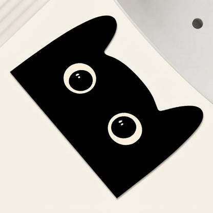 Black cat-shaped bath mat with lying cat face, big white eyes and dot nose