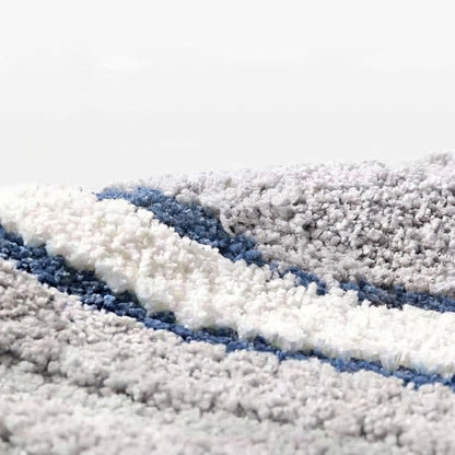 Close-up of tufted wave stripe bath mat loops in gray, white, and blue bands.
