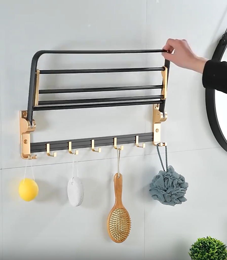 Wall-mounted towel rack with slatted shelf, gold hooks, black bars, hanging loofas