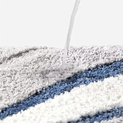 Tufted wave stripe bath mat with water poured onto gray and blue striped pile.