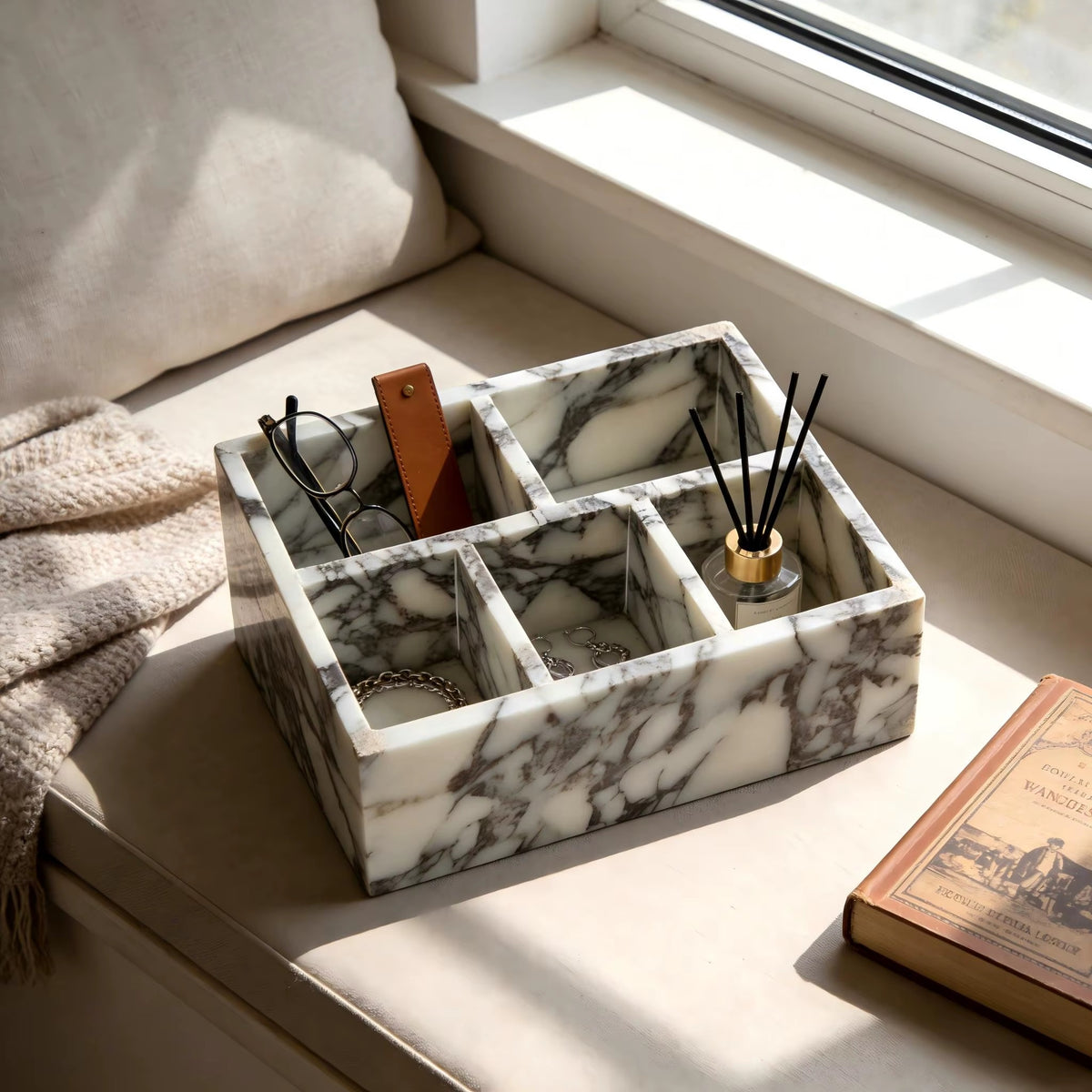 Calacatta marble makeup organiser with four compartments holding brushes and cards near window.
