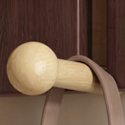 Close-up of a light gold hook with round knob on dark walnut arched wood panel