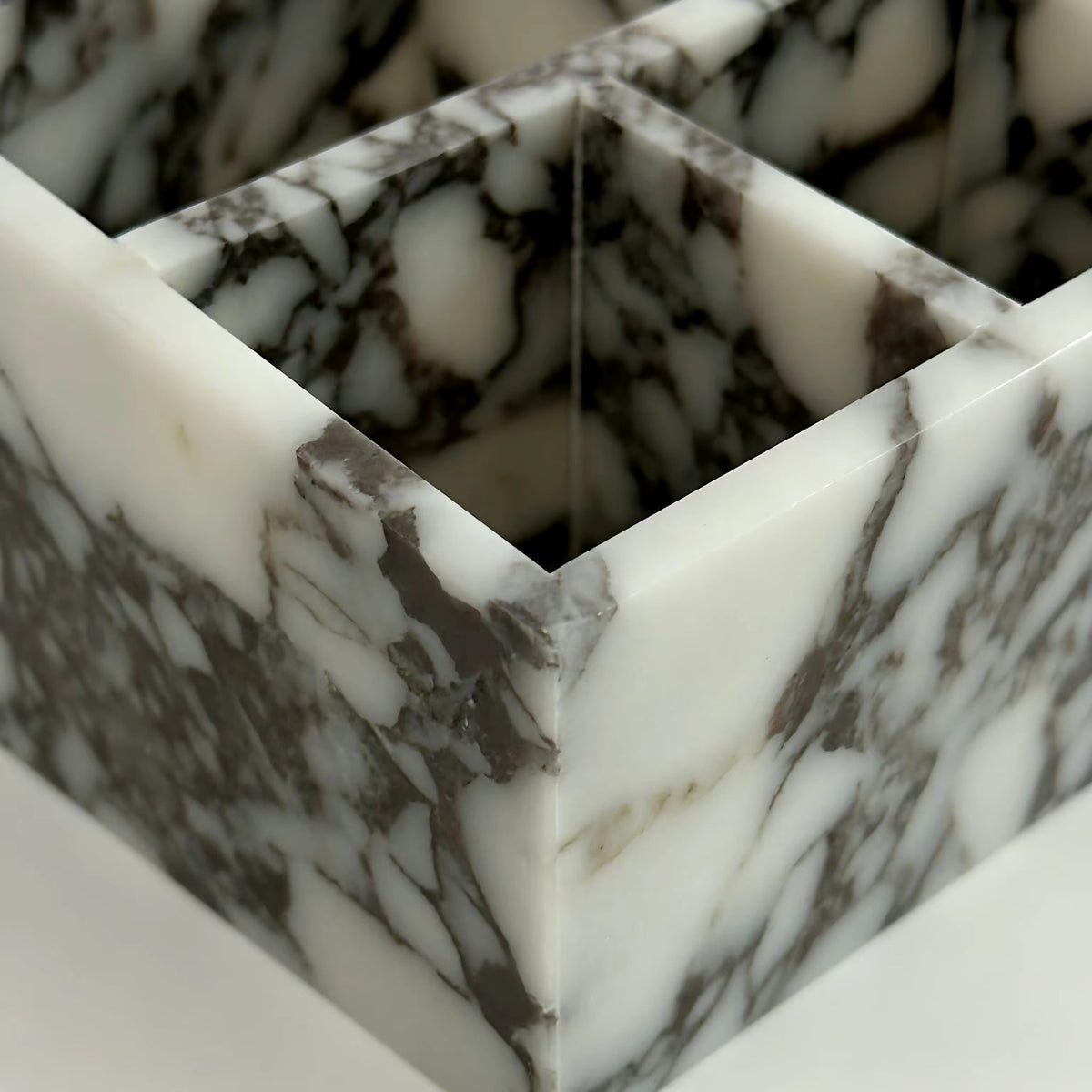 Close-up of Calacatta marble organiser with angled divider walls and veined texture.