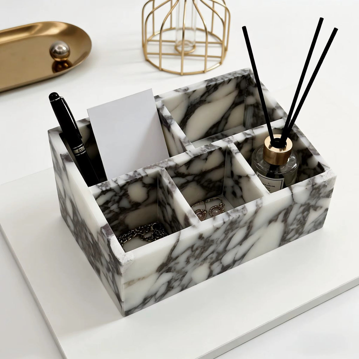 Marble makeup organiser with four square sections holding skincare bottles and reed diffuser.